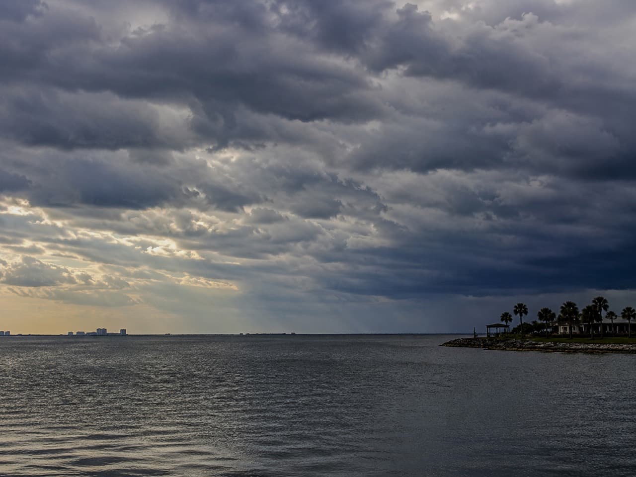 Dark storm clouds building over Mobile Bay water near the shoreline.